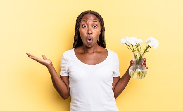 Luciendo sorprendido y conmocionado, con la mandíbula caída sosteniendo un objeto con una mano abierta en el costado. concepto de flores decorativas