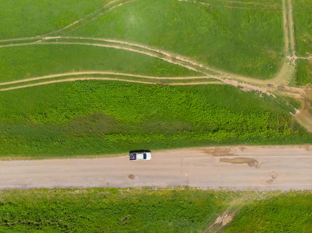 Luft-Draufsicht-Schotterweg unter der grünen Wiese mit kleinem Auto auf der Straße