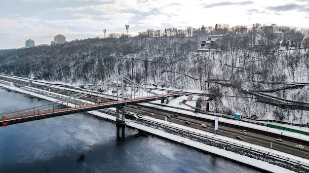 Luftansicht der Fußgängerparkbrücke im Winter und im Dnjepr von oben, Schnee Kiew Stadtbild, Stadt Kiew Skyline, Ukraine