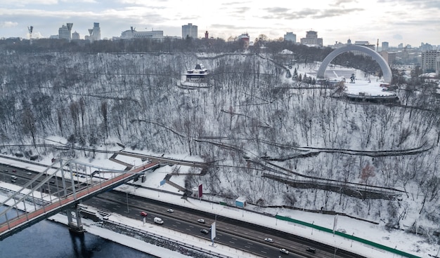 Luftansicht der Fußgängerparkbrücke im Winter und im Dnjepr von oben, Schnee Kiew Stadtbild, Stadt Kiew Skyline, Ukraine