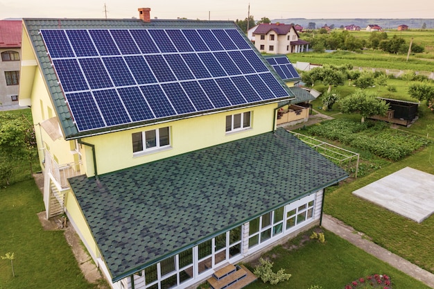 Luftansicht des neuen modernen Wohnhaushauses mit blau glänzendem Solarfoto-Voltaik-Paneelsystem auf Dach. Konzept zur Erzeugung erneuerbarer ökologischer grüner Energie.