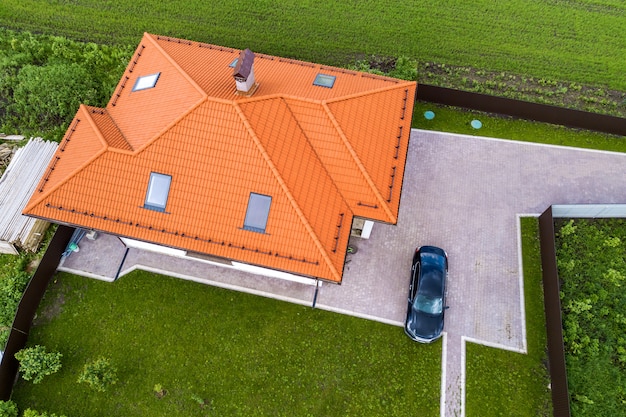 Luftansicht des Schindeldachs des Hauses mit Dachfenstern und schwarzem Auto auf Hof