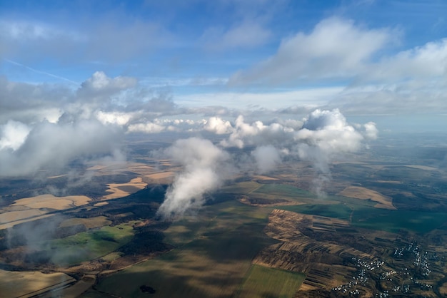 Luftaufnahme aus großer Höhe der fernen Stadt, die mit geschwollenen Cumulus-Wolken bedeckt ist, die sich vor Regensturm bilden Flugzeugsicht auf bewölkte Landschaft