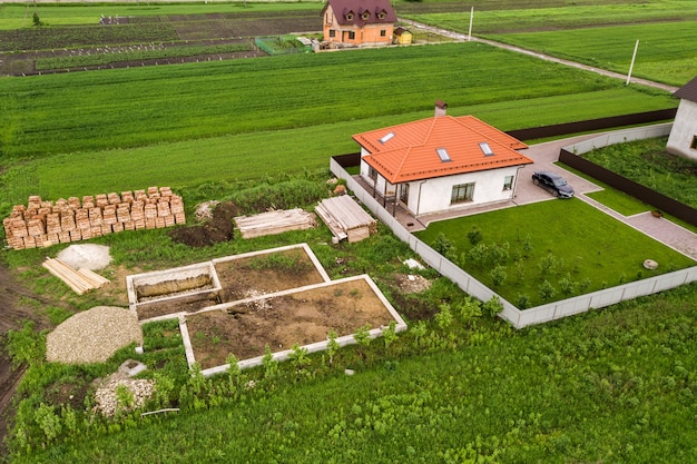 Luftaufnahme der Baustelle für zukünftiges Backsteinhaus, Betonfundamentboden und Stapel gelber Lehmziegel für den Bau.