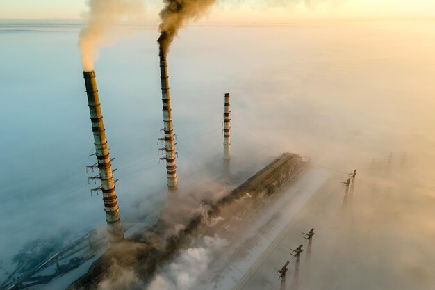 Luftaufnahme der hohen Rohre des Kohlekraftwerks mit schwarzem Rauch, der bei Sonnenuntergang die umweltverschmutzende Atmosphäre aufsteigt.