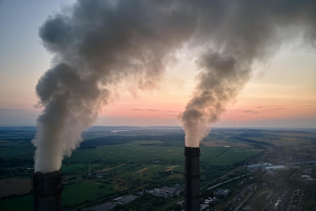 Luftaufnahme der hohen Rohre des Kohlekraftwerks mit schwarzem Rauch, der sich bei Sonnenuntergang nach oben bewegt und die Atmosphäre verschmutzt. Erzeugung elektrischer Energie mit fossilem Brennstoffkonzept