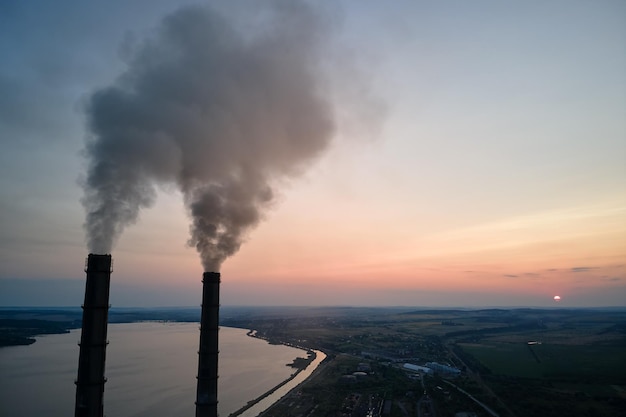 Luftaufnahme der hohen Rohre des Kohlekraftwerks mit schwarzem Rauch, der sich bei Sonnenuntergang nach oben bewegt und die Atmosphäre verschmutzt. Erzeugung elektrischer Energie mit fossilem Brennstoffkonzept