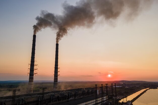 Luftaufnahme der hohen Rohre des Kohlekraftwerks mit schwarzem Rauch, der sich bei Sonnenuntergang nach oben bewegt und die Atmosphäre verschmutzt Produktion von elektrischer Energie mit fossilem Brennstoffkonzept