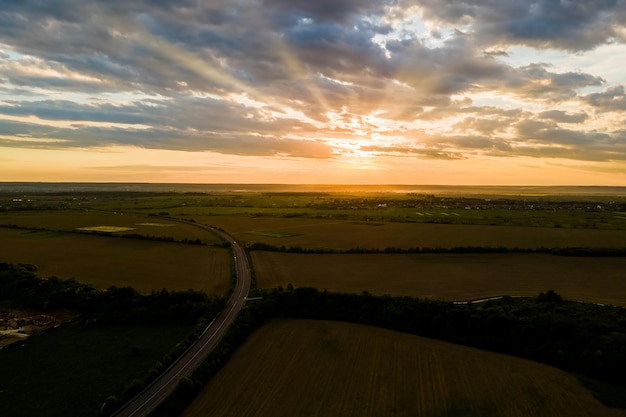 Luftaufnahme der Intercity-Straße mit schnell fahrenden Autos zwischen Ackerlandfeldern bei Sonnenuntergang. Draufsicht von der Drohne des Autobahnverkehrs am Abend.