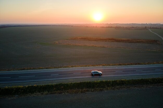 Luftaufnahme der Intercity-Straße mit unscharfem, schnell fahrendem Auto bei Sonnenuntergang. Draufsicht von der Drohne des Autobahnverkehrs am Abend.