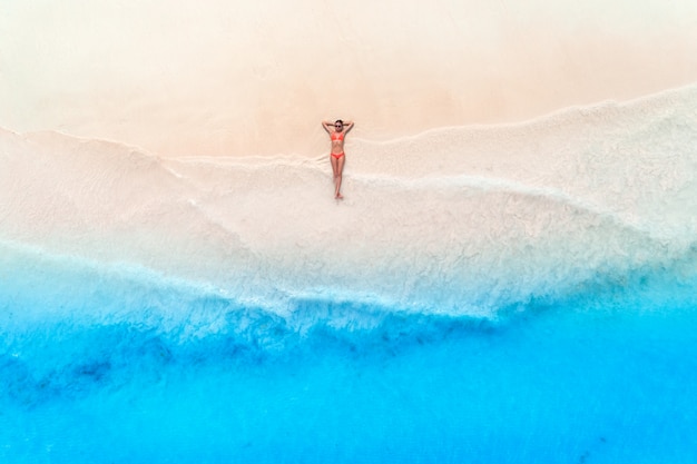 Luftaufnahme der jungen Frau, die auf dem weißen Sandstrand liegt