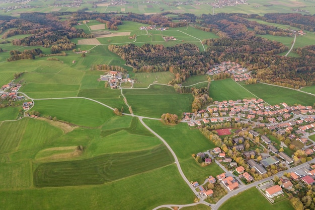 Luftaufnahme der kleinen Stadt mit roten Ziegeldächern zwischen grünen Bauernfeldern und entferntem Wald im Sommer.