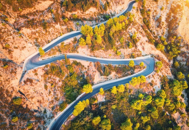 Luftaufnahme der kurvenreichen Straße in wunderschönen Bergen bei Sonnenuntergang im Herbst Draufsicht der Bergstraße im Wald Bunte Landschaft mit Straßenbäumen mit grünen und orangefarbenen Blättern im Herbst Reisen Sie in die Natur