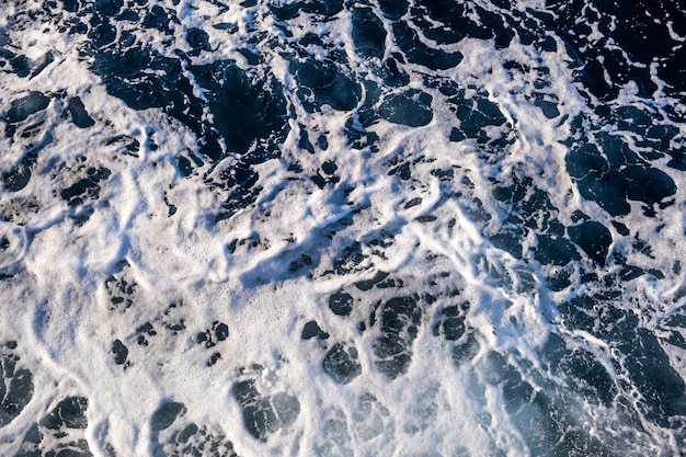 Luftaufnahme der Meerwasseroberfläche von oben nach unten. Weißer Schaumwellenbeschaffenheit als natürlicher Hintergrund.