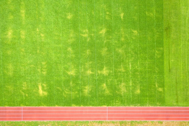 Luftaufnahme der oberfläche des grünen, frisch geschnittenen grases auf dem fußballstadion mit roten laufbahnen im sommer
