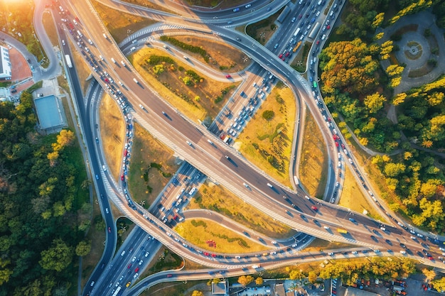 Foto luftaufnahme der straße in der modernen stadt bei sonnenuntergang im sommer. blick von oben auf den verkehr im autobahnkreuz. landschaft mit autos auf erhöhter straße, grüne bäume. kreuzungsüberführung. belebte kreuzung. hauptverkehrszeit