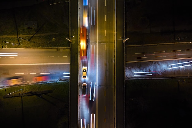 Luftaufnahme der Straßenkreuzung mit schnellem Verkehr in der Nacht. Draufsicht des städtischen Verkehrs. Hauptverkehrszeit mit Bewegungsunschärfe-Autospurlichtern.