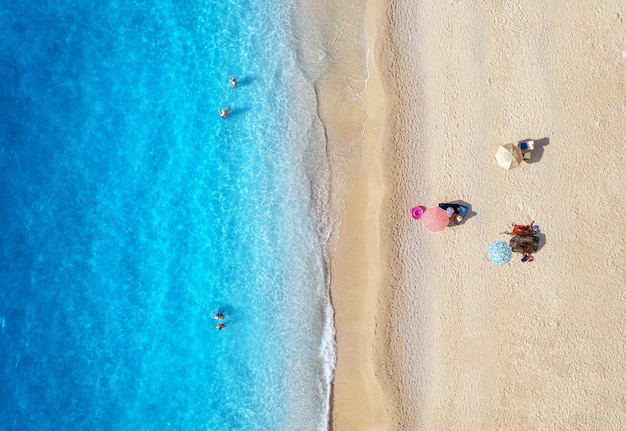 Luftaufnahme der Wellen des adriatischen Meeres, Sandstrand und Sonnenschirme mit liegenden Menschen bei Sonnenuntergang im Sommer. Tropische Landschaft mit klarem türkisfarbenem Wasser. Draufsicht von der Drohne aus. Lefkada-Insel, Griechenland-Reise