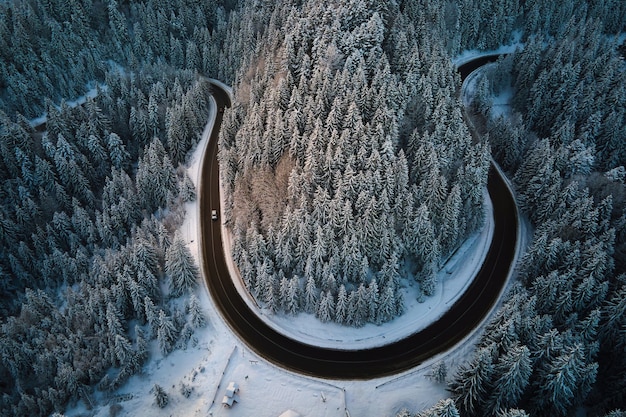 Luftaufnahme der Winterlandschaft mit schneebedeckten Berghügeln und kurvenreicher Forststraße am Morgen.