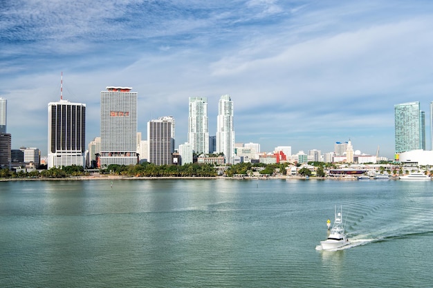 Luftaufnahme der Wolkenkratzer von Miami mit blauem, bewölktem, himmelweißem Boot, das neben der Innenstadt von Miami segelt