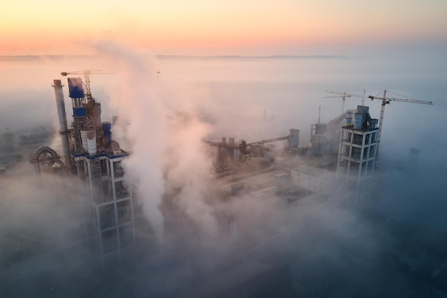 Luftaufnahme der Zementfabrik mit hoher Betonwerksstruktur und Turmkran am industriellen Produktionsstandort am nebligen Morgen Herstellung und globales Industriekonzept