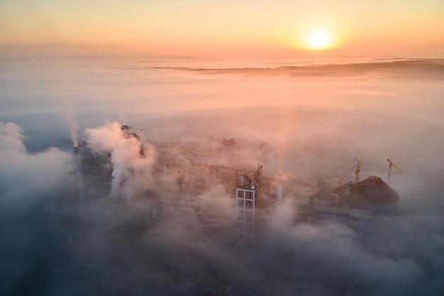 Luftaufnahme der Zementfabrik mit hoher Betonwerksstruktur und Turmkran am industriellen Produktionsstandort am nebligen Morgen Herstellung und globales Industriekonzept