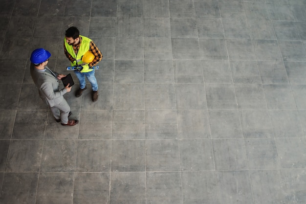 Luftaufnahme des Architekten und des Bauarbeiters, die vor Ort stehen und über Projekt diskutieren