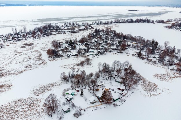 Luftaufnahme des Dorfes mitten in einem zugefrorenen Bach am Wintertag nach Schneefall