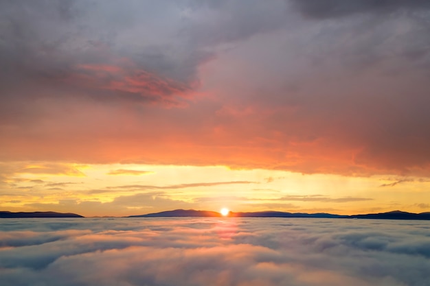 Luftaufnahme des gelben Sonnenuntergangs über weißen geschwollenen Wolken mit fernen Bergen am Horizont.