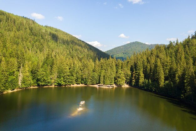 Luftaufnahme des großen Sees mit klarem blauem Wasser zwischen hohen Berghügeln, die mit dichtem immergrünen Wald bedeckt sind.