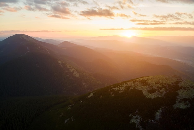 Luftaufnahme des hellen, nebligen Morgens über dunklem Gipfel mit Bergwaldbäumen bei Herbstsonnenaufgang. Schöne Landschaft des wilden Waldes im Morgengrauen