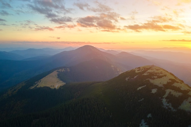 Luftaufnahme des hellen, nebligen Morgens über dunklem Gipfel mit Bergwaldbäumen bei Herbstsonnenaufgang Schöne Landschaft des wilden Waldes im Morgengrauen