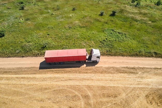 Luftaufnahme des Lastwagens, der auf unbefestigten Straßen zwischen landwirtschaftlichen Weizenfeldern fährt Transport von Getreide nach der Ernte durch Mähdrescher während der Erntesaison