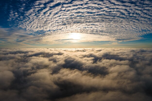 Luftaufnahme des leuchtend gelben Sonnenaufgangs über weißen dichten Wolken mit blauem Himmel oben.