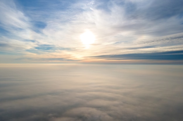 Luftaufnahme des leuchtend gelben Sonnenaufgangs über weißen dichten Wolken mit blauem Himmel oben.