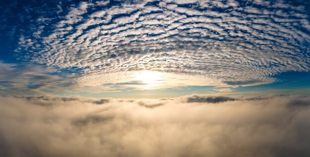 Luftaufnahme des leuchtend gelben Sonnenuntergangs über weißen dichten Wolken mit blauem Himmel oben.