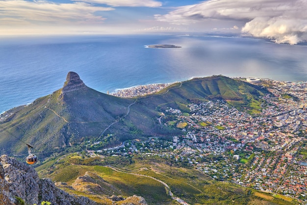 Luftaufnahme des Lions Head Mountain mit dem Ozean und einem bewölkten Himmel kopieren Raum Schöne Landschaft von grünen Bergen mit Vegetation rund um eine städtische Stadt in Kapstadt Südafrika