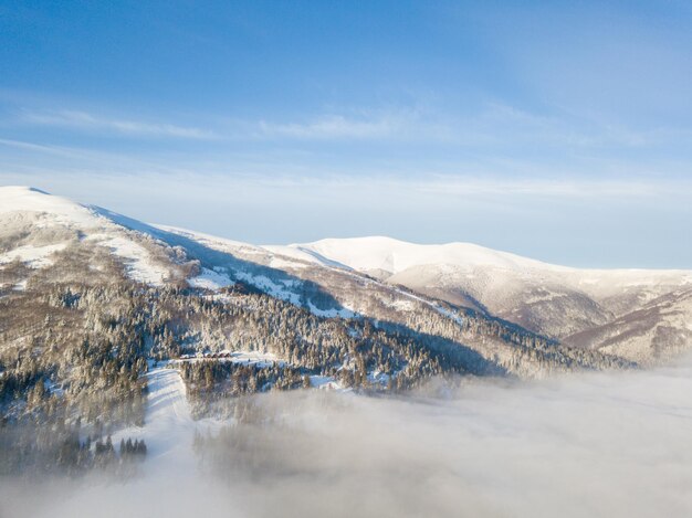 Luftaufnahme des majestätischen Sonnenaufgangs in den Bergen. Das Tal zwischen den Bergen ist mit Nebel bedeckt und wird von den warmen Strahlen der aufgehenden Sonne beleuchtet. Berge mit natürlichem Wald bedeckt