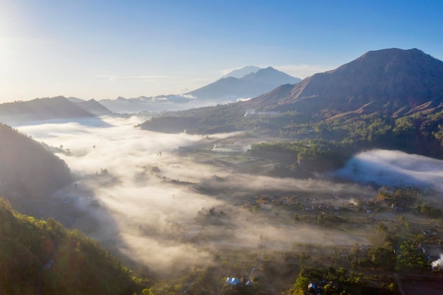 Luftaufnahme des nebligen Pinggan-Dorfes bei Sonnenaufgang mit dem Batur-Berg im Hintergrund auf Bali, Indonesien