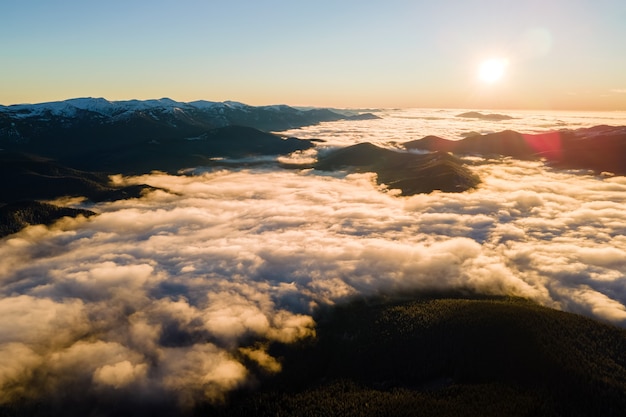 Luftaufnahme des pulsierenden Sonnenaufgangs über weißen dichten Wolken mit entfernten dunklen Bergen am Horizont.