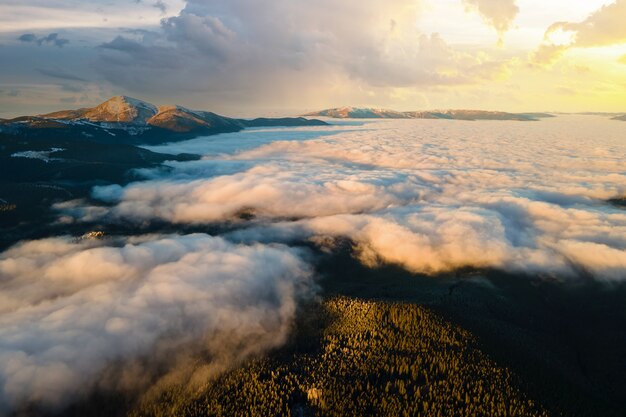 Luftaufnahme des pulsierenden Sonnenaufgangs über weißen dichten Wolken mit entfernten dunklen Bergen am Horizont.