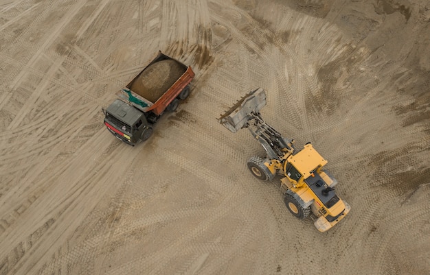 Luftaufnahme des Sandsteinbruchs. Bulldozer gießt Sand in LKW