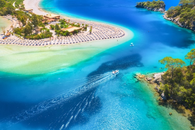 Luftaufnahme des Sandstrandes, blaues Meer, Schnellboot an einem sonnigen Tag im Sommer, Motorboot in der Blauen Lagune, Sonnenliegen, klares azurblaues Wasser, tropische Landschaft mit grünen Yachtbäumen, Draufsicht, Ölüdeniz, Türkei