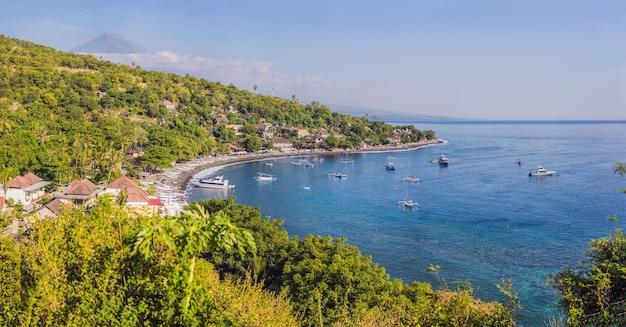 Luftaufnahme des Strandes von Amed in Bali Indonesien Traditionelle Fischerboote namens Jukung am schwarzen Sandstrand und der Vulkan Mount Agung im Hintergrund teilweise von Wolken bedeckt