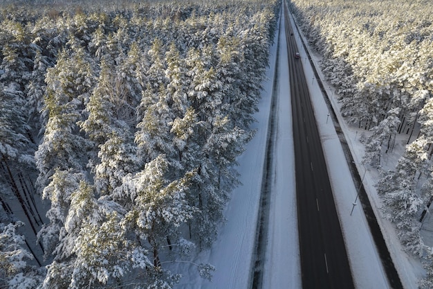 Luftaufnahme einer Asphaltstraße, die durch frostige Winterwälder und mit Schnee bedeckte Gärten führt