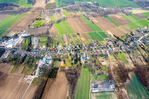 Luftaufnahme einer kleinen Stadt zwischen grünen Feldern, einem kleinen Dorf, einer langen Straße und vielen Privathäusern