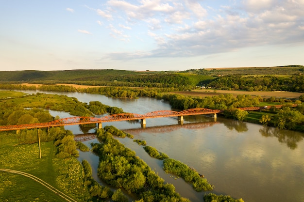 Luftaufnahme einer schmalen straßenbrücke, die sich über schlammigen breiten fluss im grünen ländlichen bereich erstreckt.