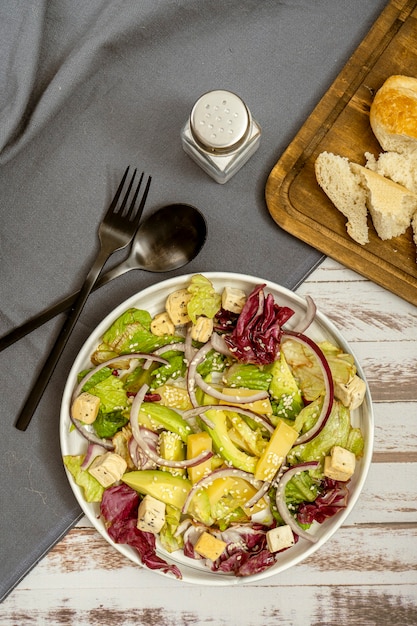 Luftaufnahme einer Schüssel mit Salat aus einer Mischung aus Salat, roten Zwiebeln, Avocado, Manchego-Käse und Croutons mit Samen und Olivenöl. vertikale Ausrichtung und Kopierbereich.