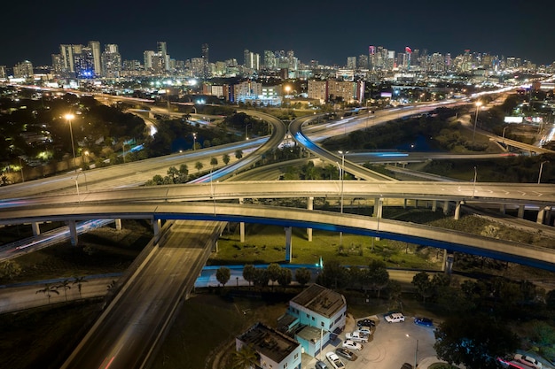 Luftaufnahme eines amerikanischen Autobahnkreuzes bei Nacht mit schnell fahrenden Fahrzeugen in Miami, Florida. Blick von oben auf die Verkehrsinfrastruktur der USA