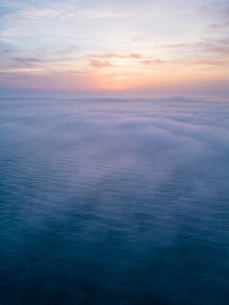 Luftaufnahme eines aufgehenden Meeres mit einer Decke aus Morgennebel und morgendlichen Sonnenstrahlen